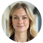 صورة شخصية احترافية لامرأة شقراء مبتسمة ترتدي سترة داكنة، وهي تقف في ردهة بالقرب من المكاتب.