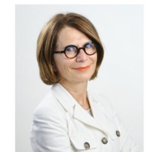 Donna con capelli castani corti e occhiali rotondi, che indossa un blazer bianco e sorride alla fotocamera.