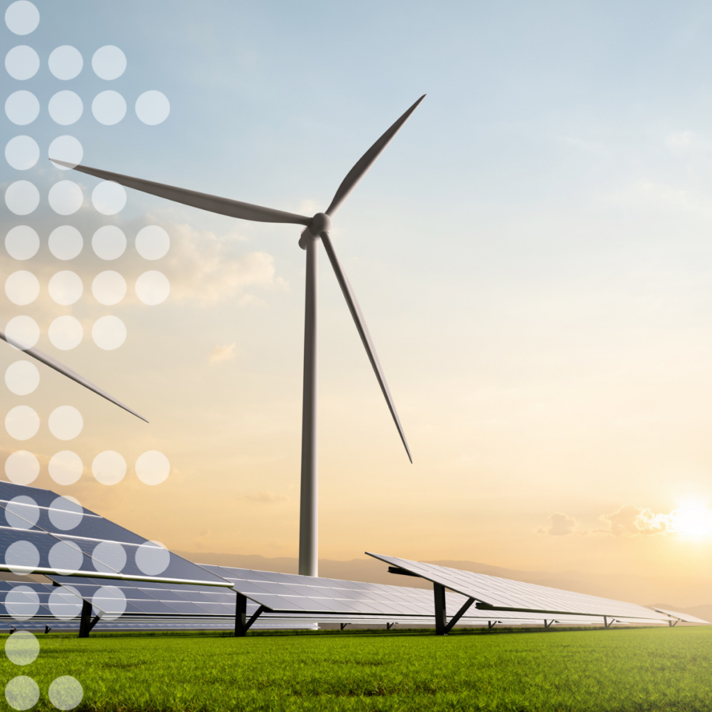 Una turbina eolica e dei pannelli solari su un prato al tramonto, a simboleggiare l'energia rinnovabile.
