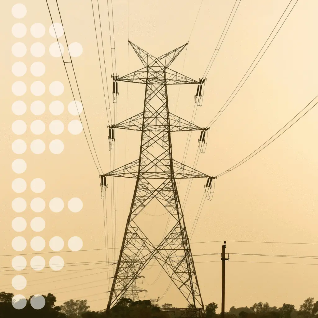 Un grand pylône électrique métallique en treillis, sur lequel s'étendent de multiples lignes électriques, se détache sur un ciel brumeux au-dessus d'un paysage rural.