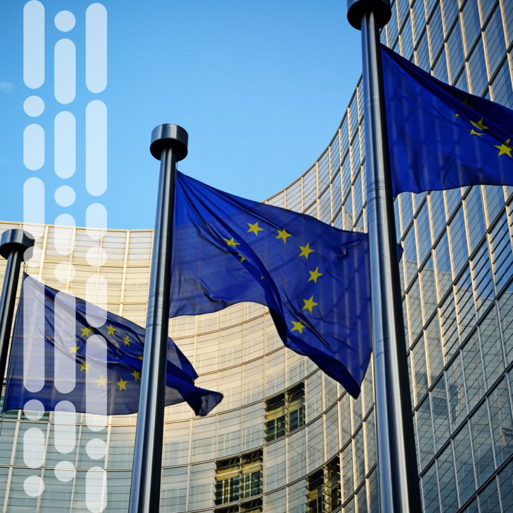 Vor einem modernen Bürogebäude aus Glas wehen vor blauem Himmel die Flaggen der Europäischen Union.